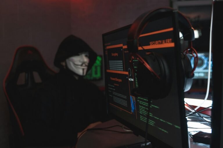 A person wearing a Guy Fawkes mask engaged in hacking activities on a computer in a dimly lit room.
